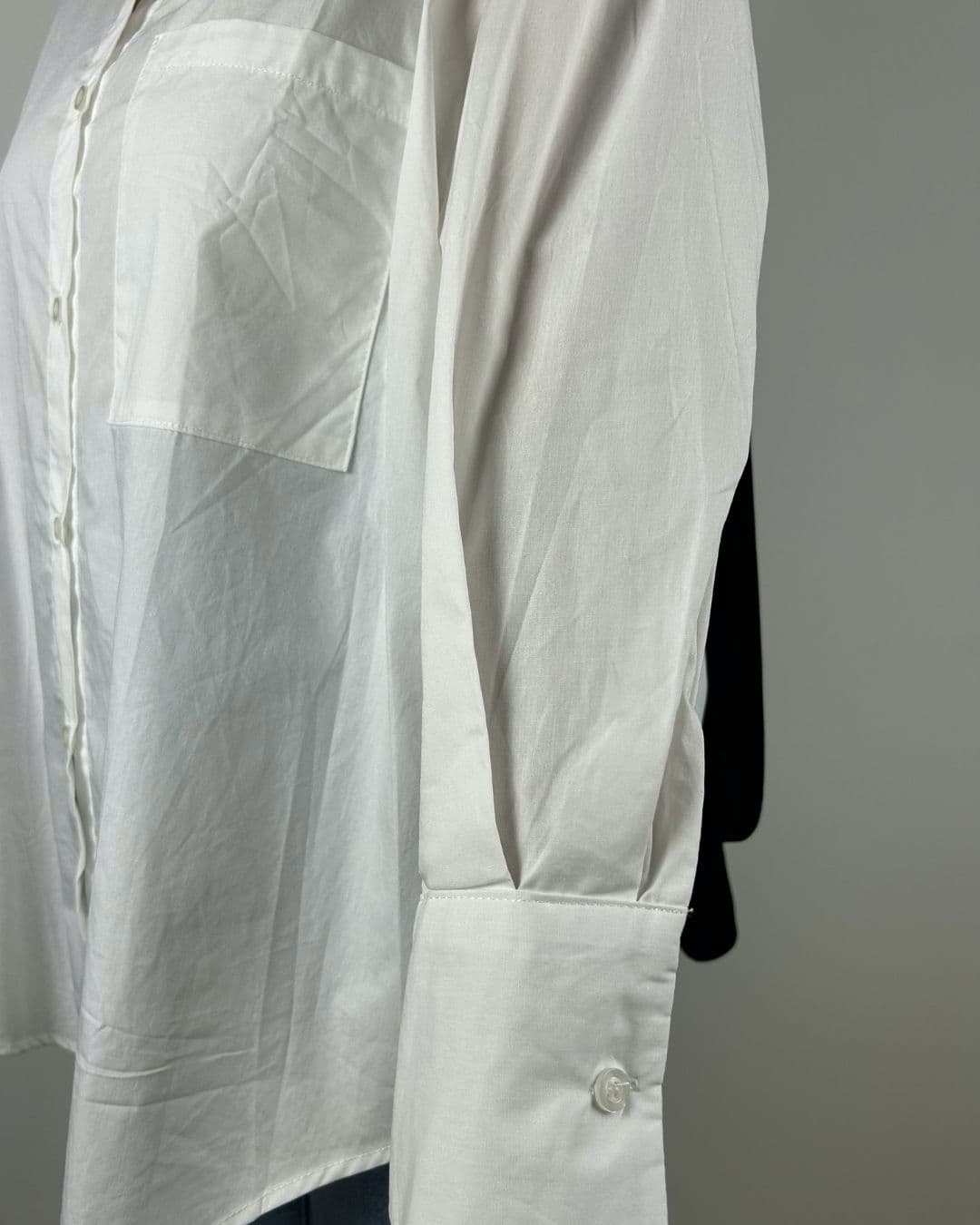 Zoom sur la manche boutonnée et la poche poitrine de la chemise oversize blanche