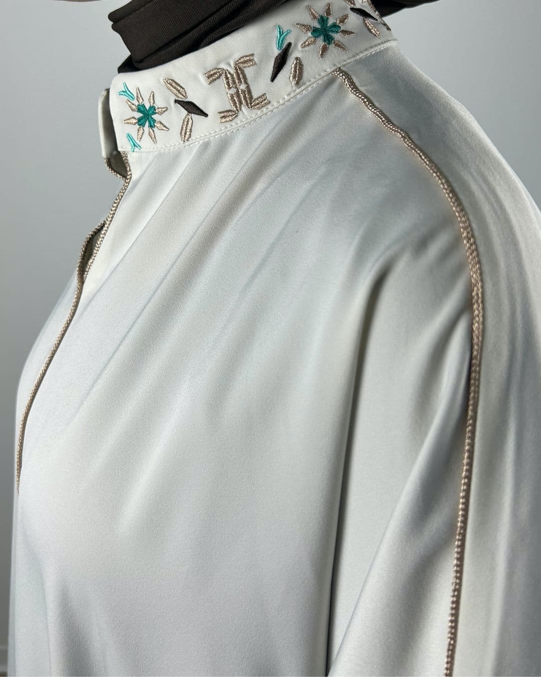 Gros plan sur le col brodé beige et turquoise d'une robe satinée écrue